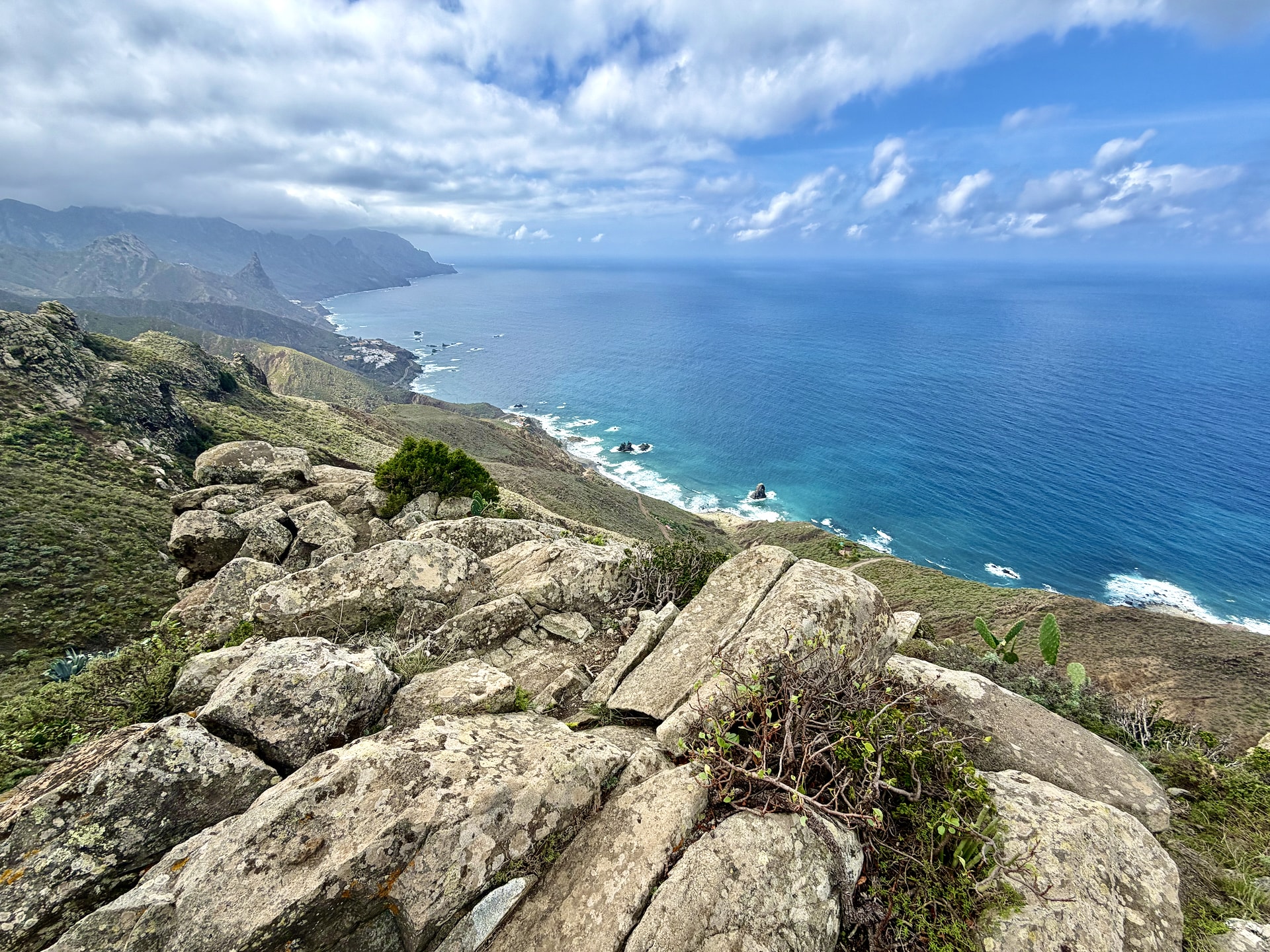 Lichen-covered boulders on the trail high above the north coast of Anaga, with the coastline, rock stacks and the Atlantic stretching away