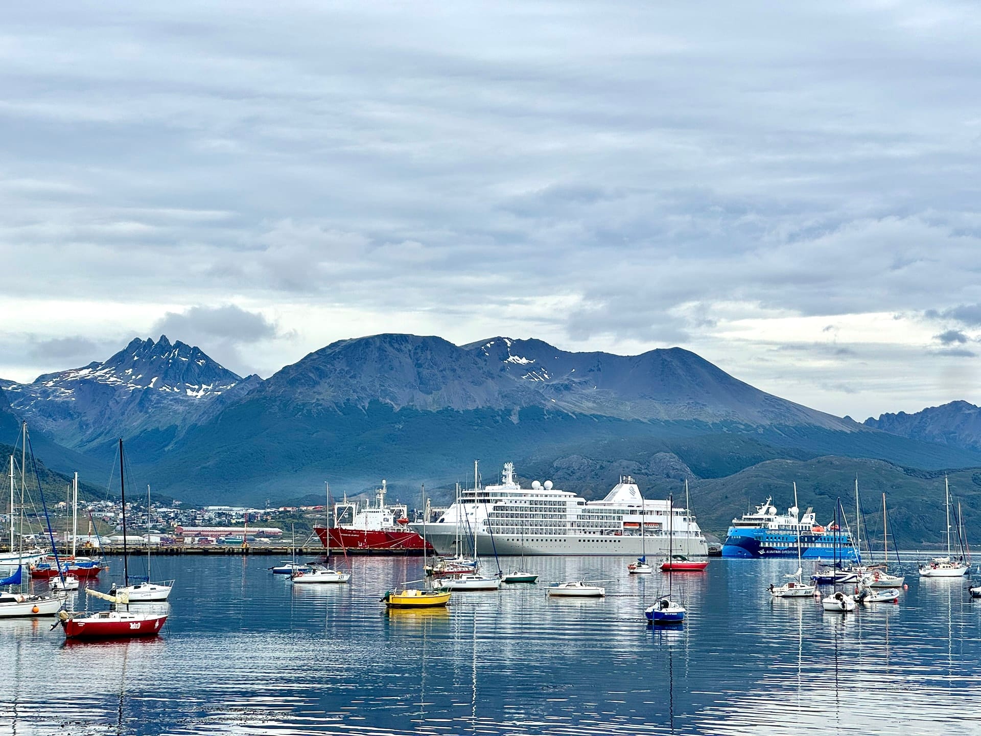Expedition ships including the blue Ocean Albatros moored in Ushuaia harbor among sailboats, mountains behind