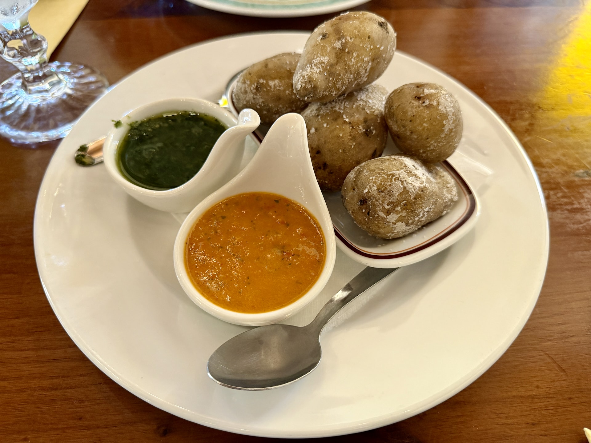 Wrinkled potatoes on a plate with small jugs of green and red mojo sauce