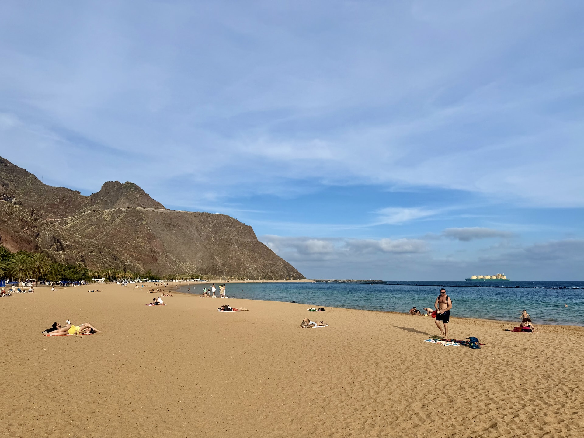 Playa de Las Teresitas golden sand beach near Santa Cruz Wide golden sand of Playa de Las Teresitas with sunbathers, a brown mountainside behind and a large tanker anchored offshore