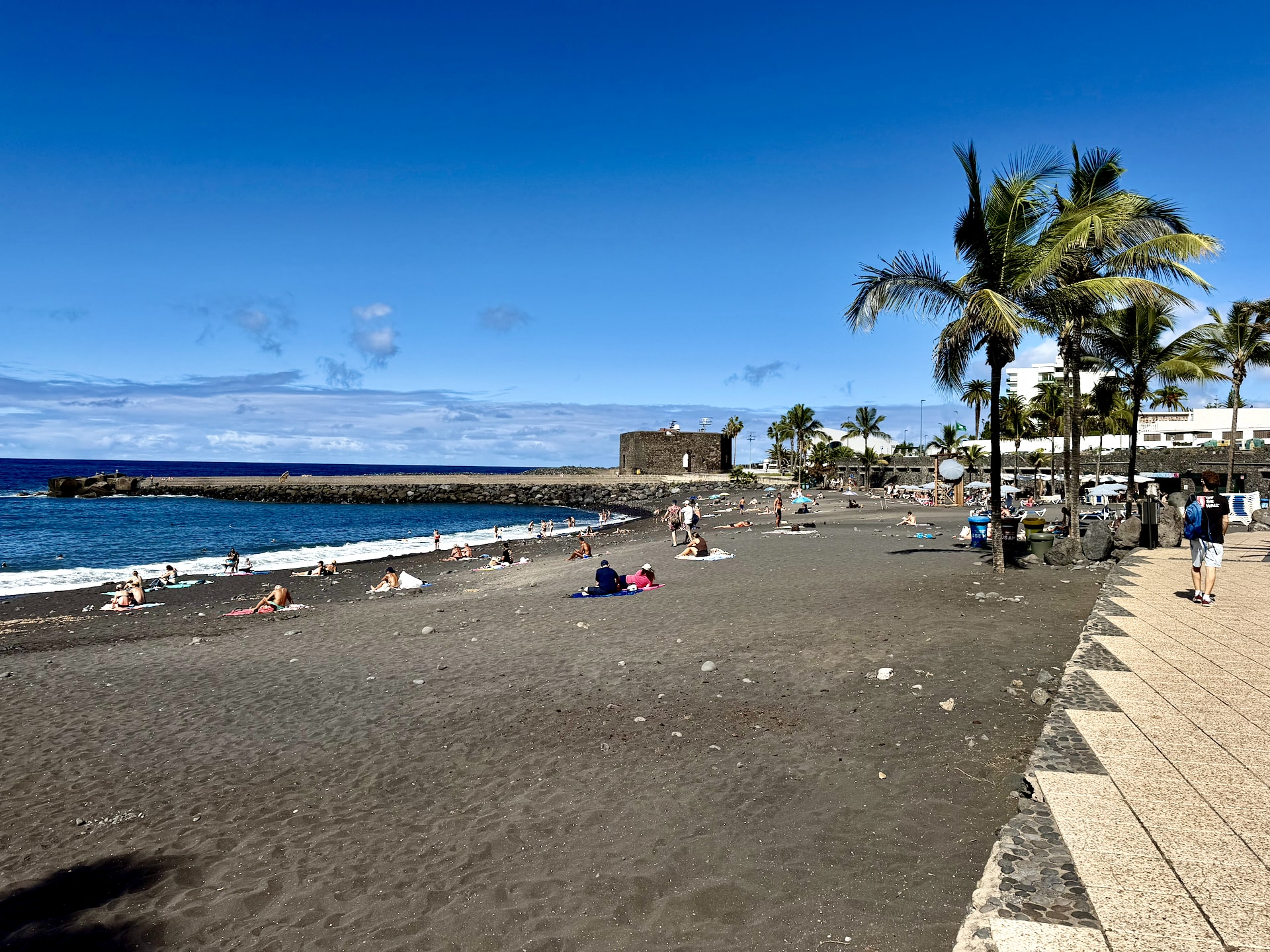 Playa Jardín black sand beach in Puerto de la Cruz Black sand of Playa Jardín in Puerto de la Cruz with sunbathers, palm trees, the promenade and the old stone Castillo de San Felipe by the sea