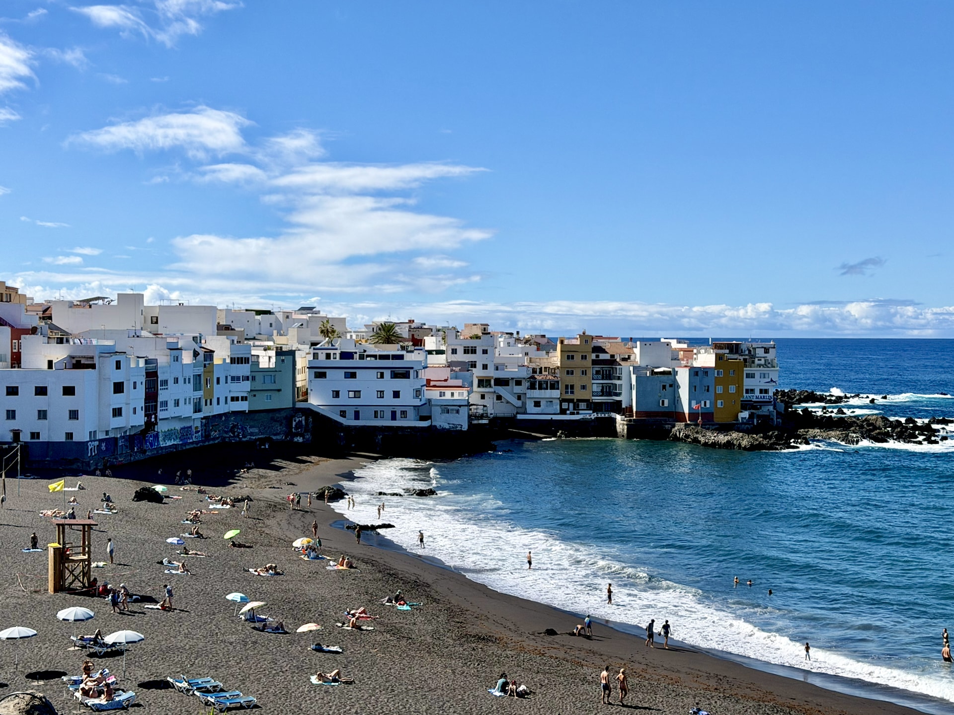 Punta Brava beach and colorful houses, Puerto de la Cruz Punta Brava's black sand beach below white and colorful apartment buildings at the water's edge, with parasols, a lifeguard tower and breaking waves