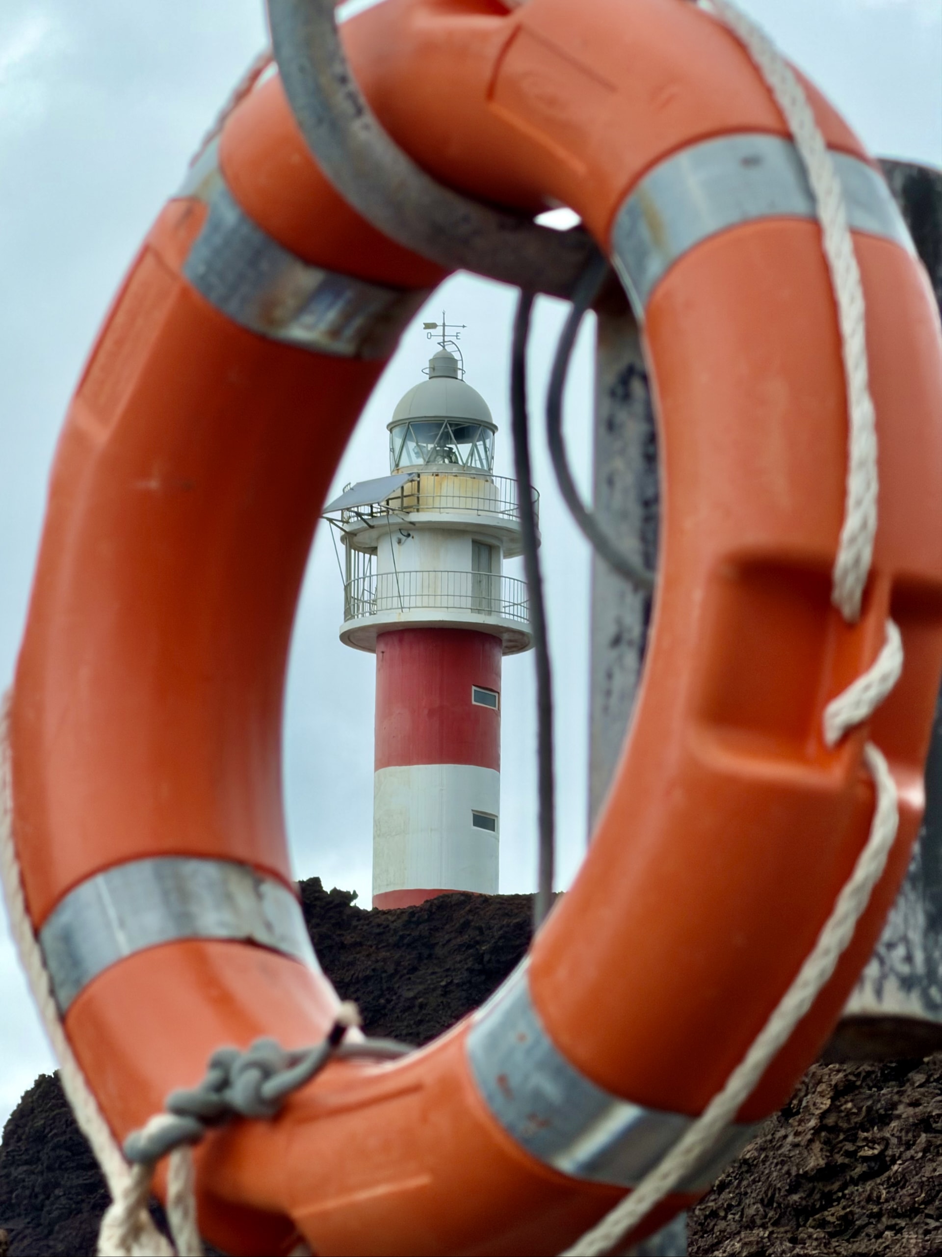 The red-and-white Punta de Teno lighthouse framed through an orange life ring