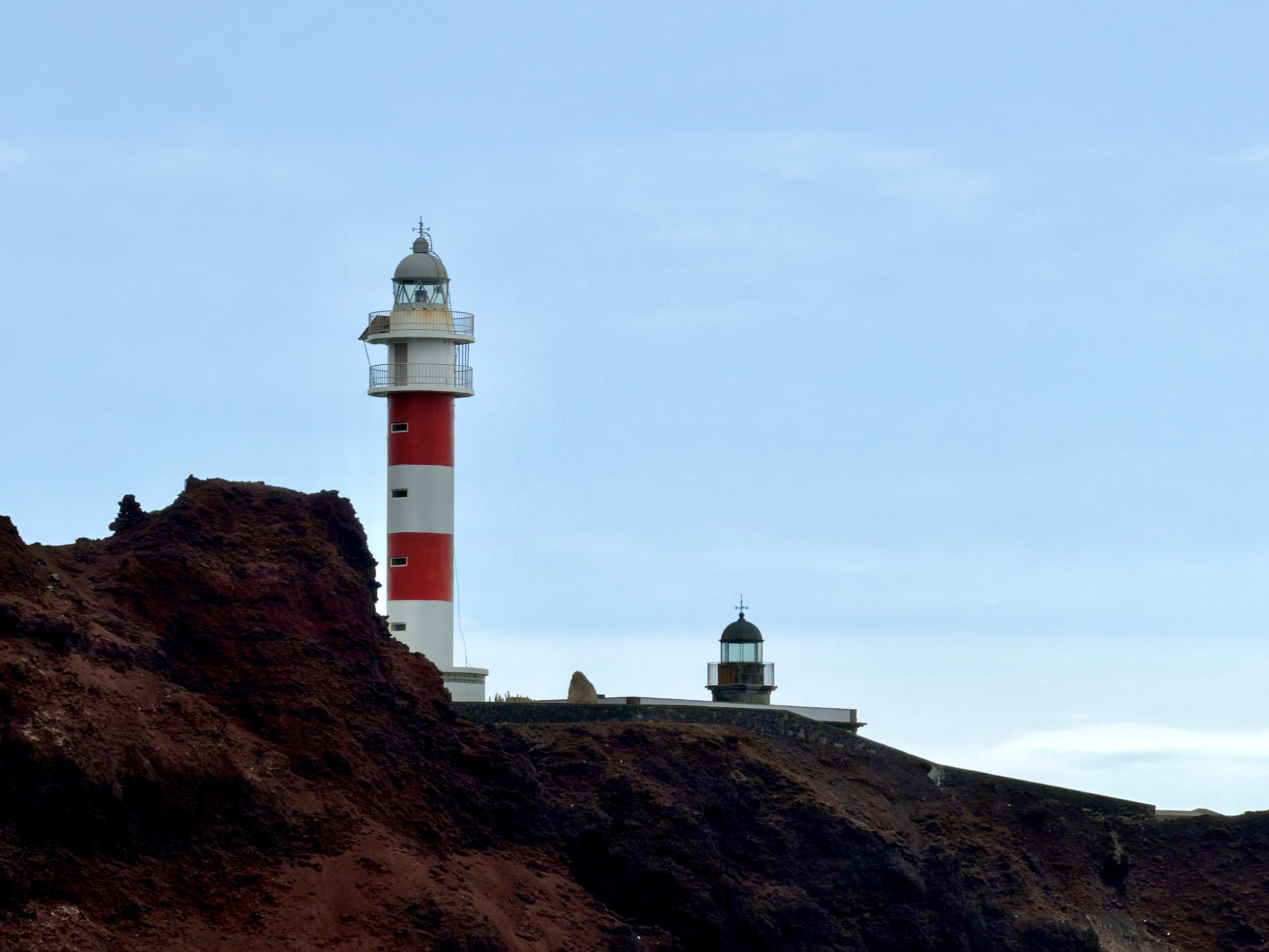 The red-and-white Punta de Teno lighthouse and the small old lighthouse beside it on a dark volcanic headland in Tenerife