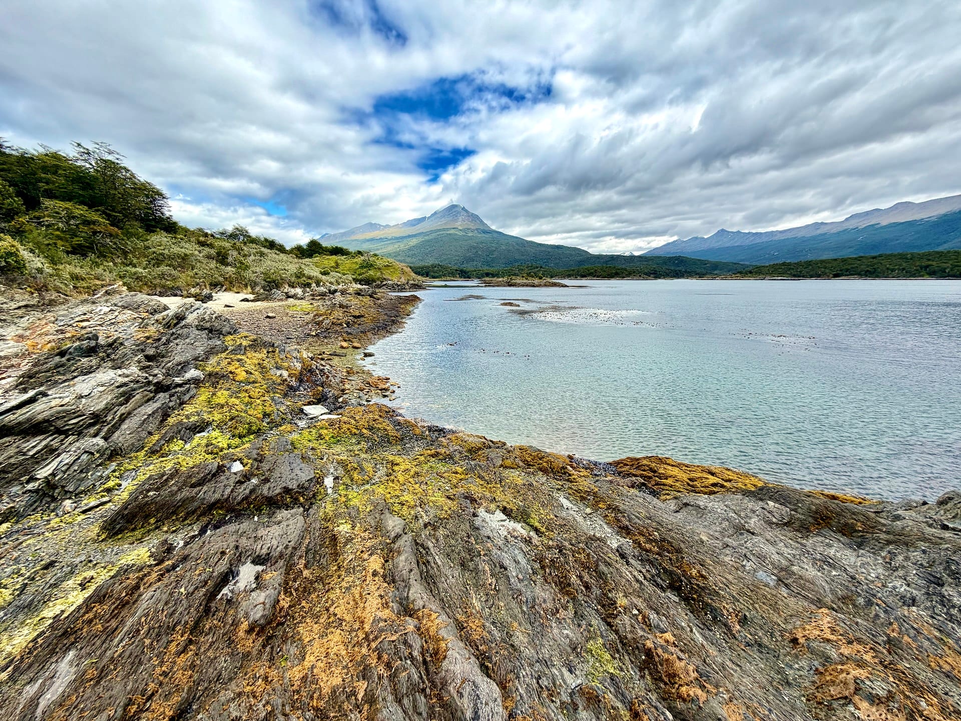 Slippery moss-covered rocks on the shore of Bahía Lapataia with mountains across the water