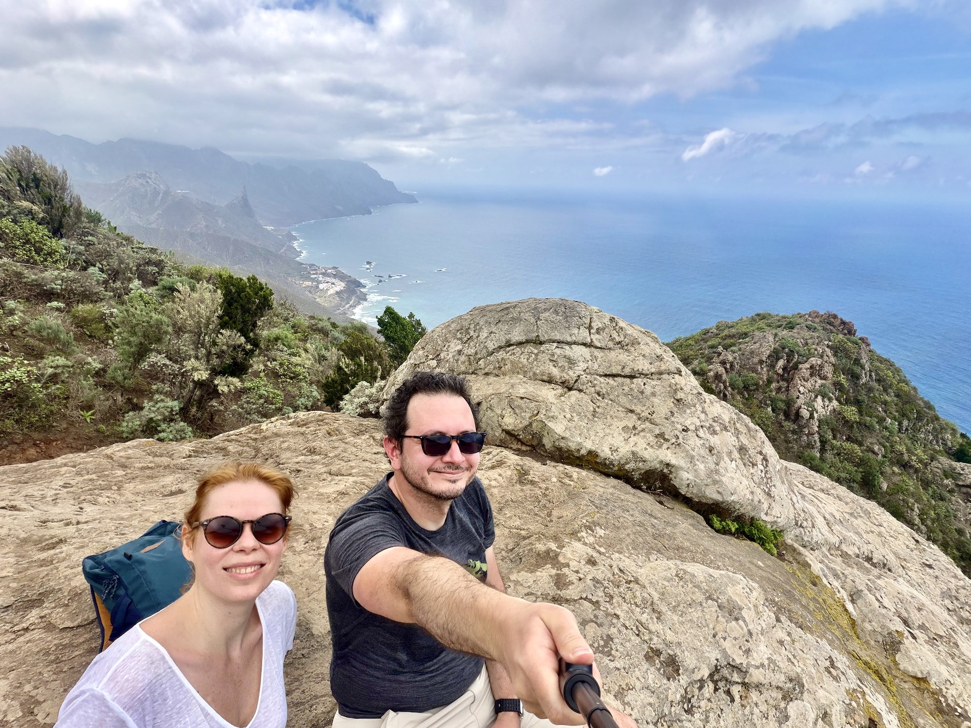 Andrea and Laszlo taking a selfie on a large rock high on the trail, with the Anaga coastline and the Atlantic behind them