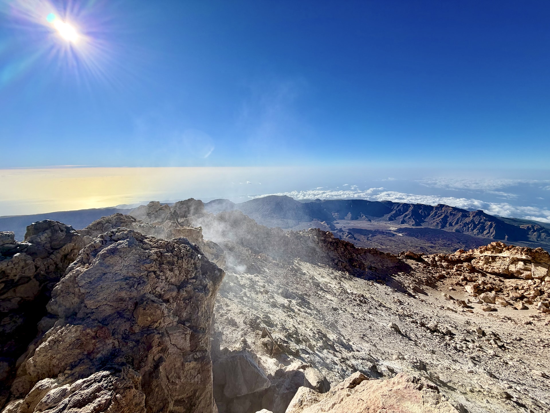 Steam rising from fumaroles among the rocks at the summit of Mount Teide, with the caldera and the sea of clouds in the background