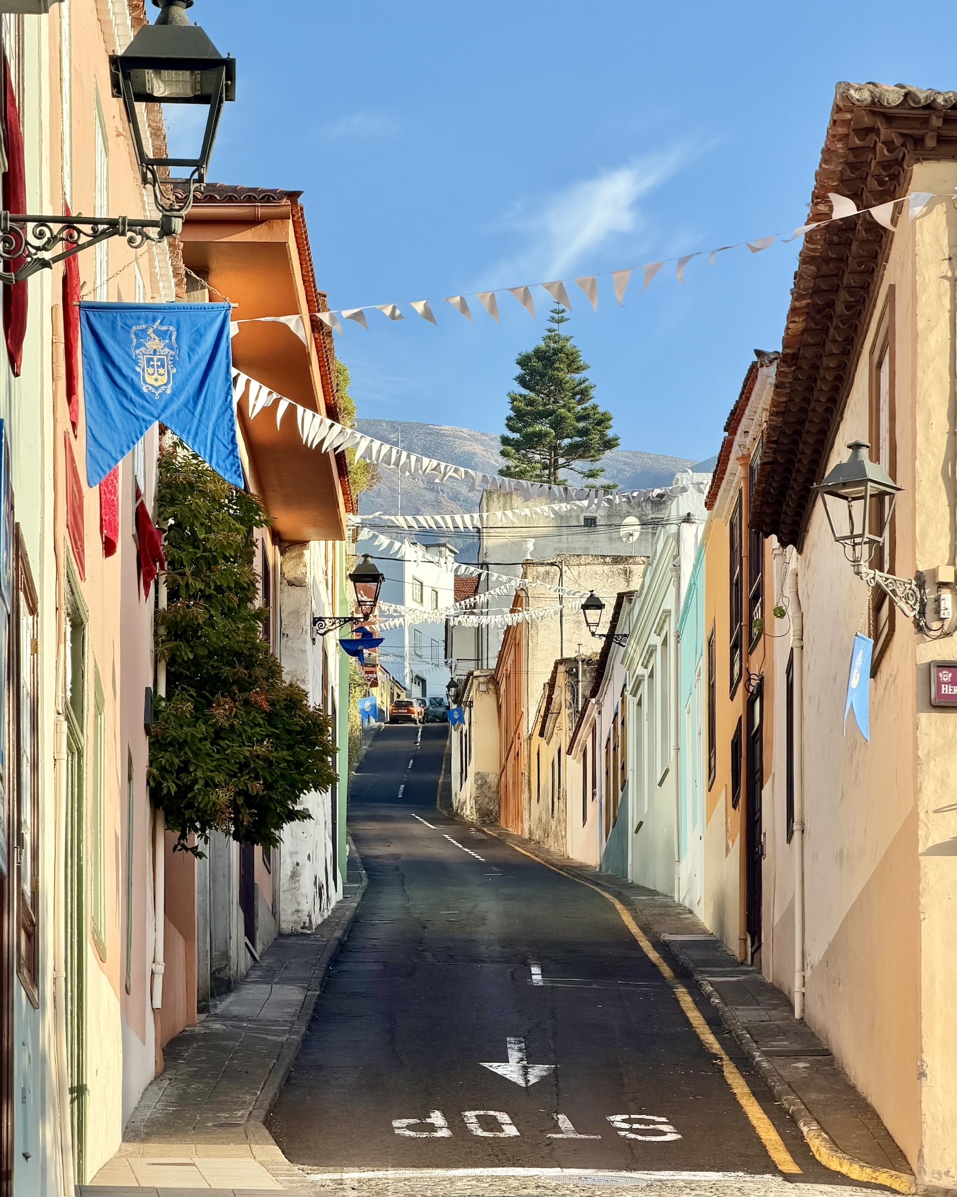 Sloping street in La Orotava's old town with pastel houses, iron lanterns and festival bunting, rising towards the hills