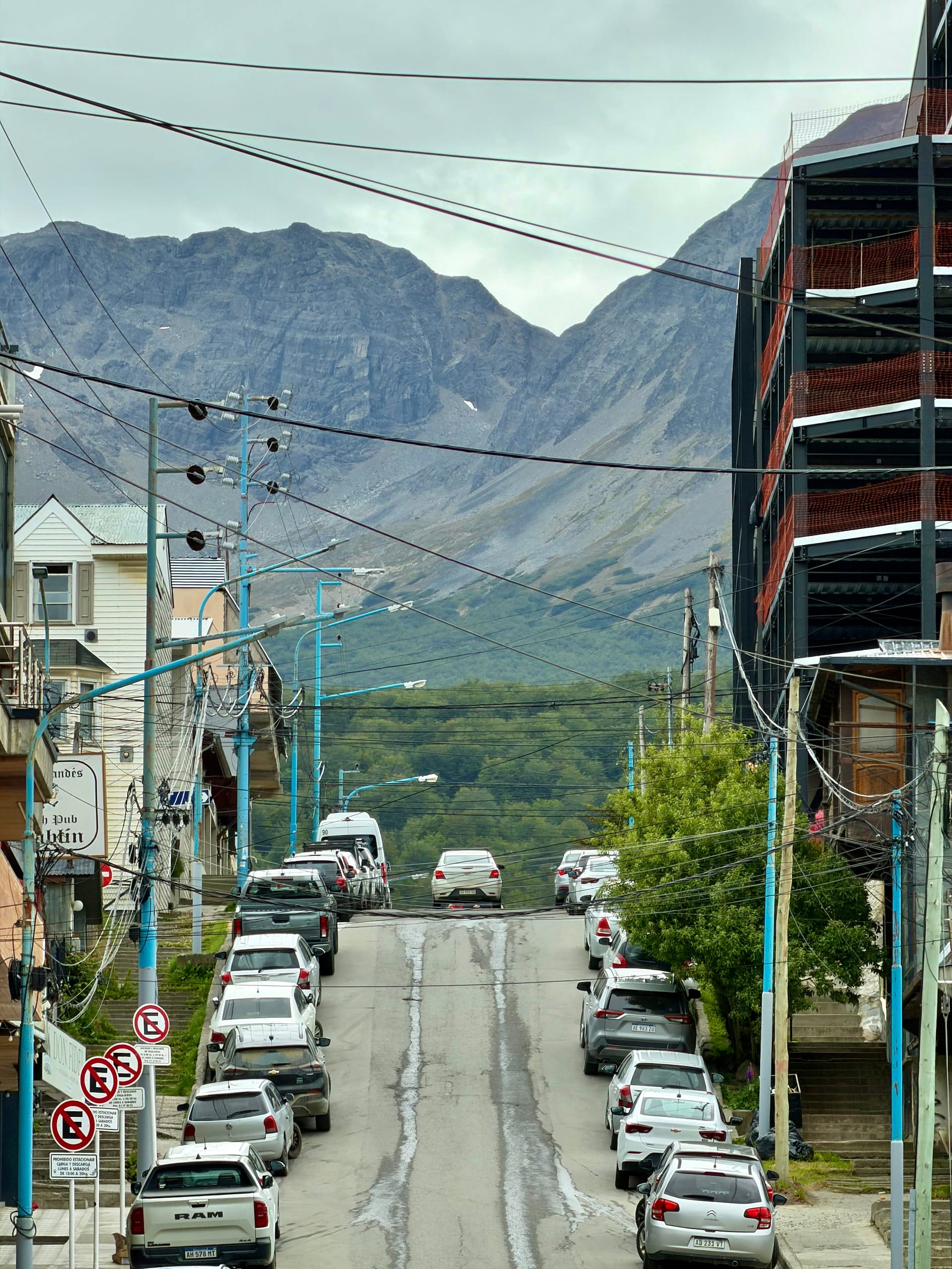Steep street lined with parked cars and power lines running uphill toward the mountains in Ushuaia