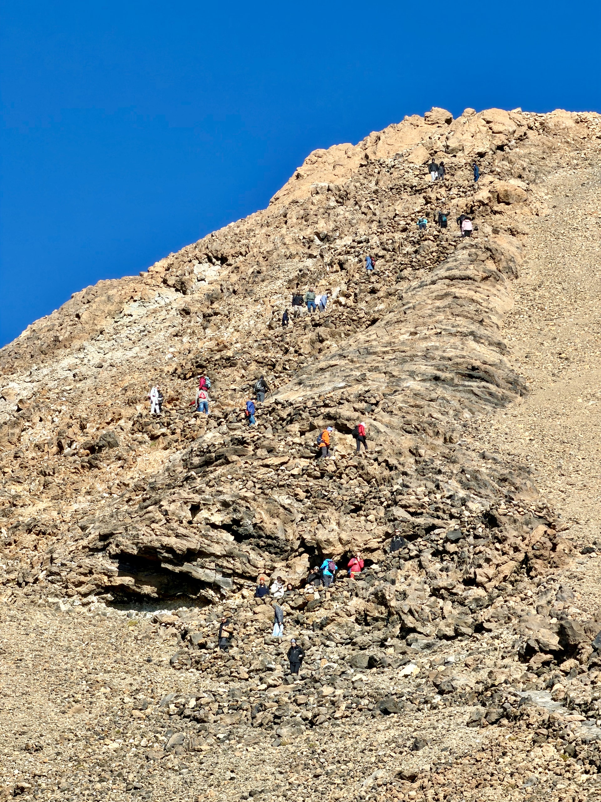 A line of hikers spread out along the steep summit trail on the upper slope of Mount Teide