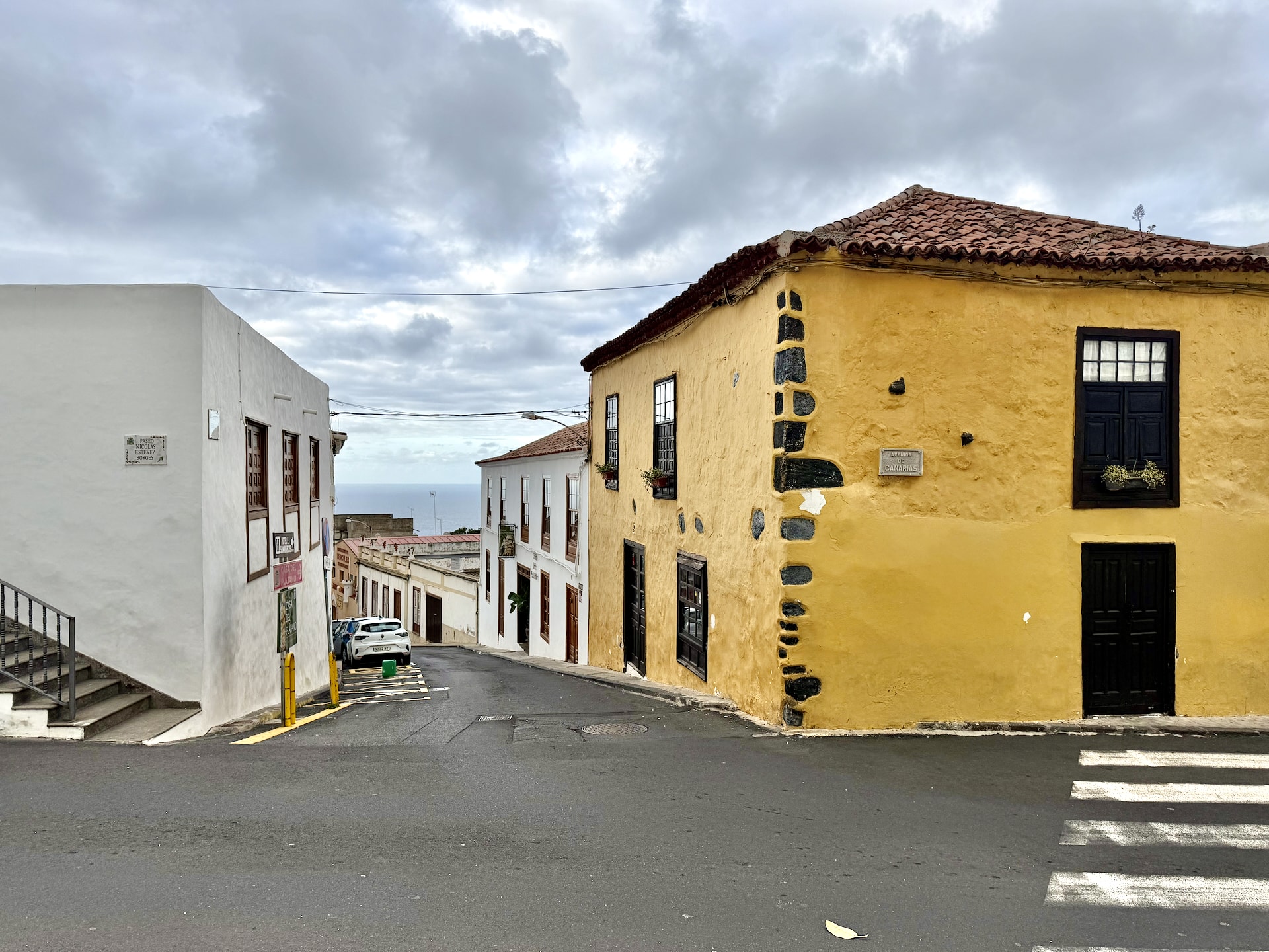 Street with a yellow corner house and white buildings leading up to the dragon tree in Icod de los Vinos