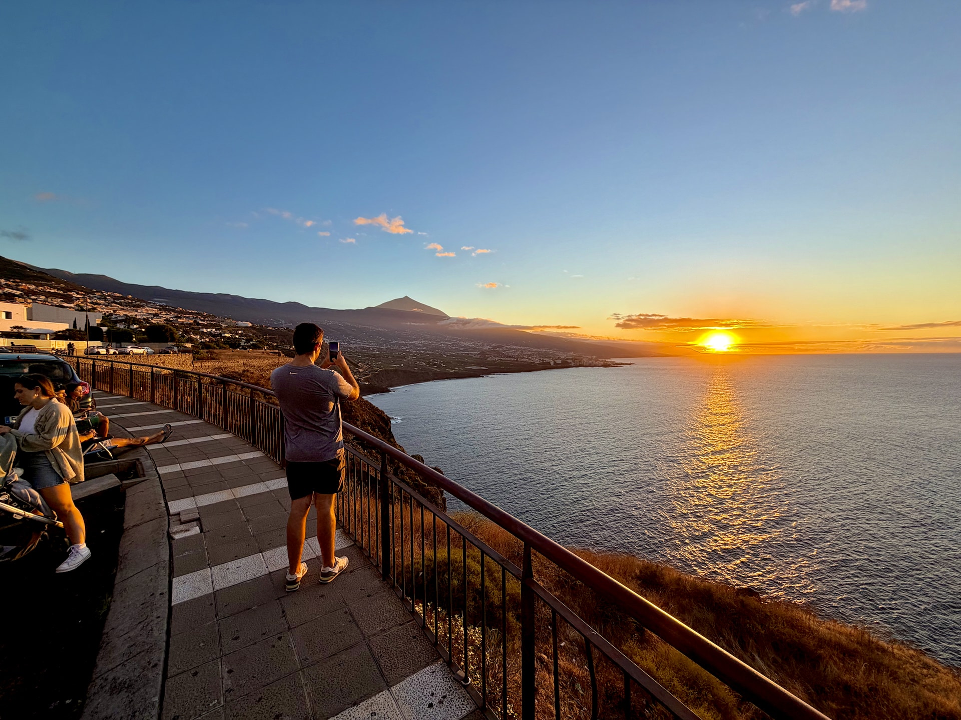 People watching the sun set over the Atlantic from the railing at Mirador de la Quinta, with Teide on the horizon