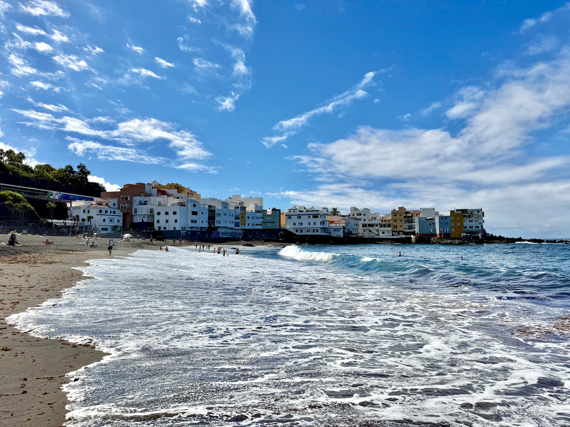 Swimmers in the waves at Punta Brava, Puerto de la Cruz Surf washing over the dark sand at Punta Brava in Puerto de la Cruz, with swimmers in the waves and colorful apartment buildings behind