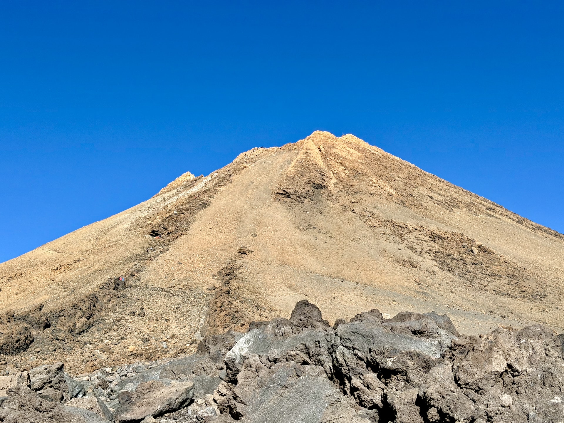 The summit cone of Mount Teide rising steeply above dark lava rocks against a clear blue sky