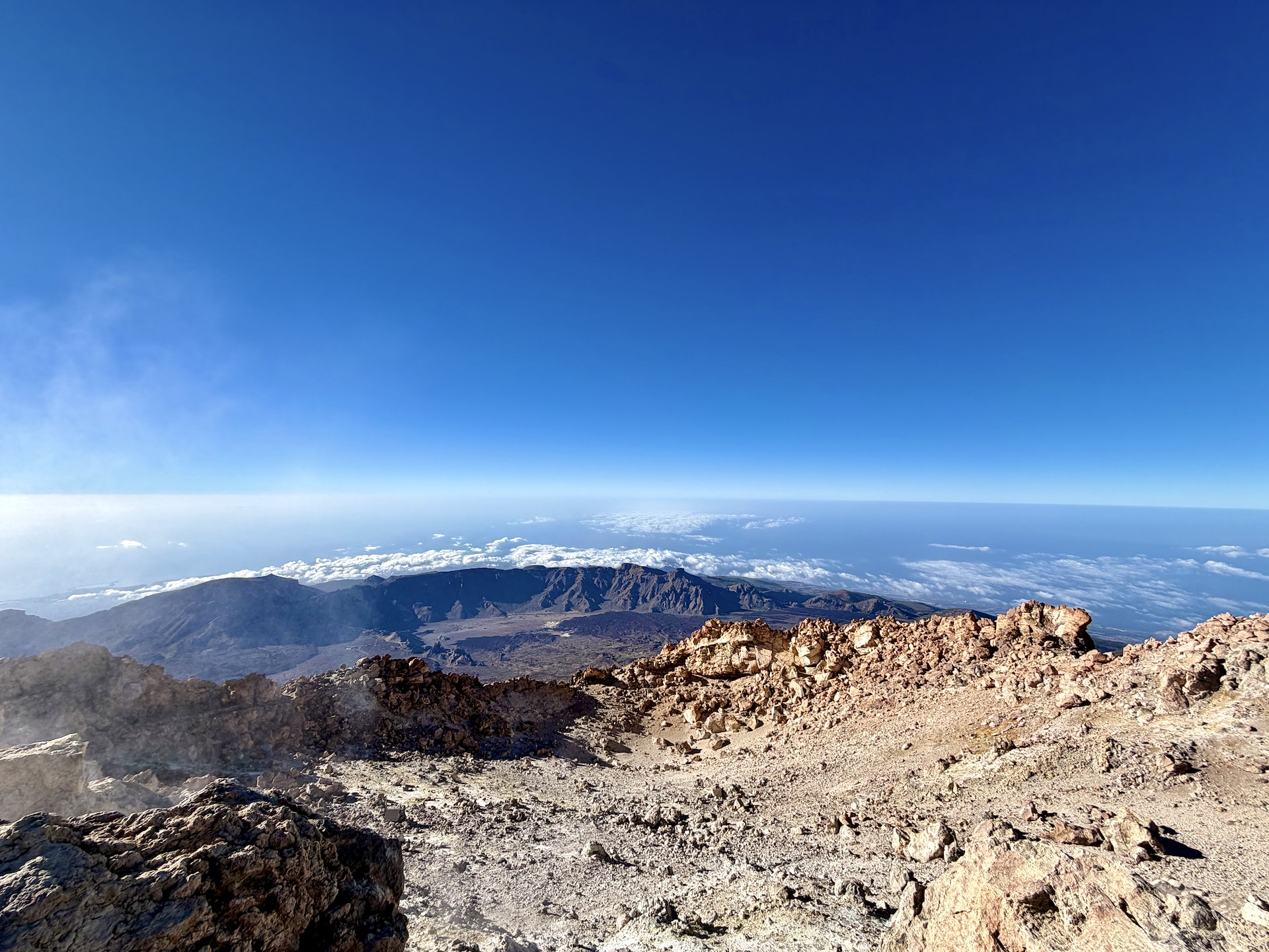 The shallow summit crater of Mount Teide, a hollow of pale rock and scattered steam, with the sea of clouds on the horizon