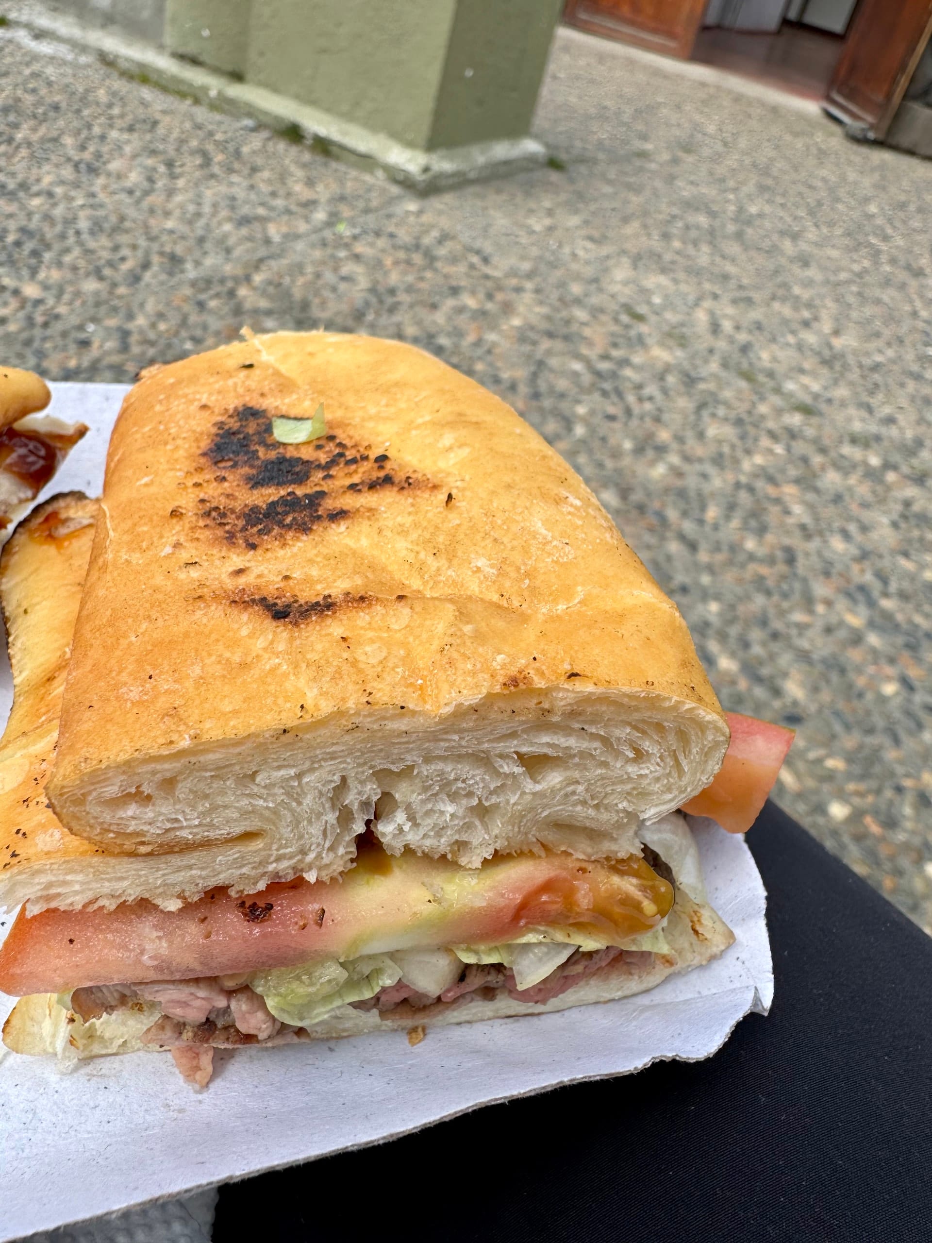 Toasted sandwich with meat, tomato and lettuce on a paper wrapper