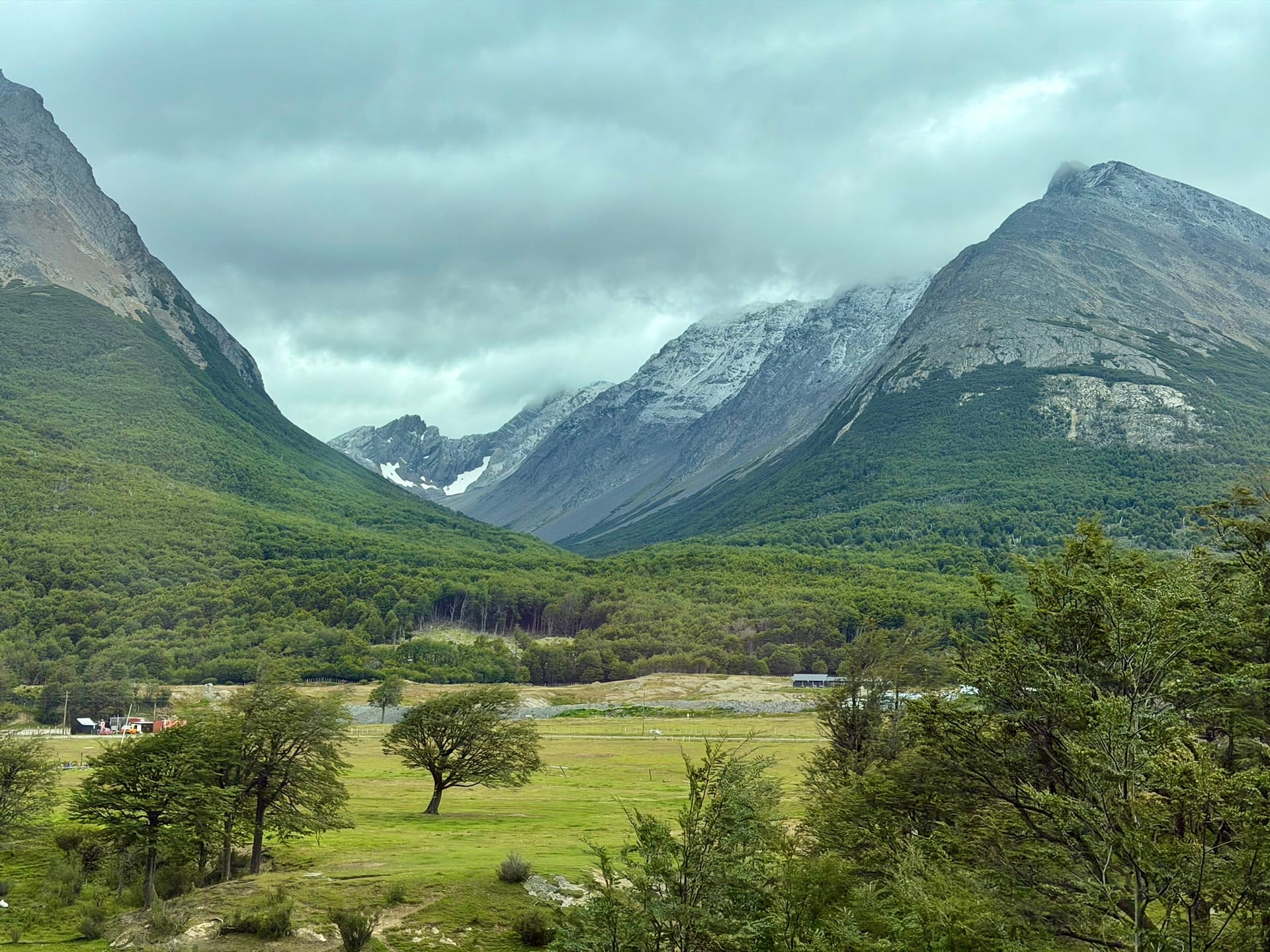 Green valley with scattered trees and snow-dusted mountains on the drive to Tierra del Fuego National Park
