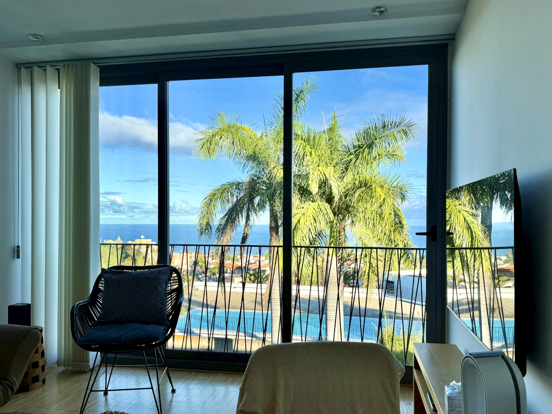 View from the living room of an apartment in La Quinta, Santa Úrsula: floor-to-ceiling windows, palm trees, the pool and the Atlantic Ocean beyond
