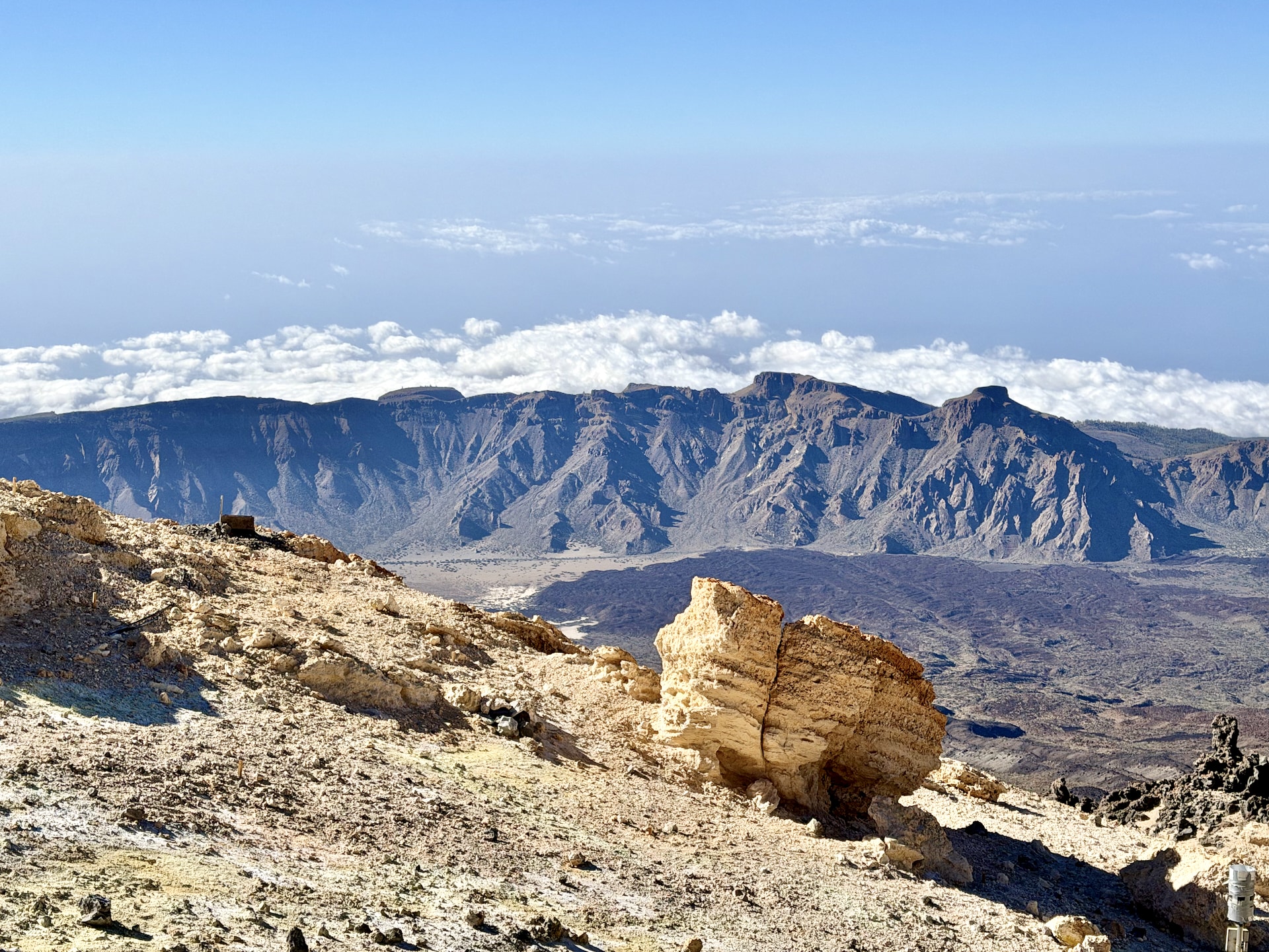 A pale eroded rock formation on the upper slopes of Mount Teide, with the caldera wall and a band of clouds in the distance